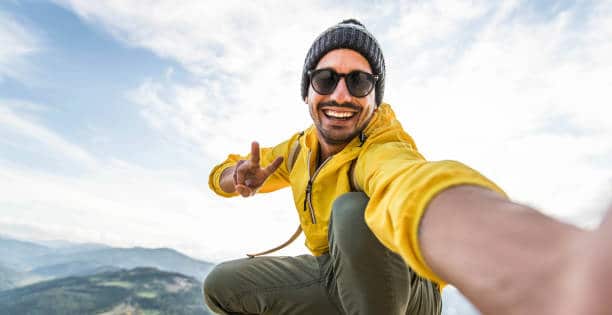 Smiling man in early 30s wearing sunglasses and taking selfie while hiking.