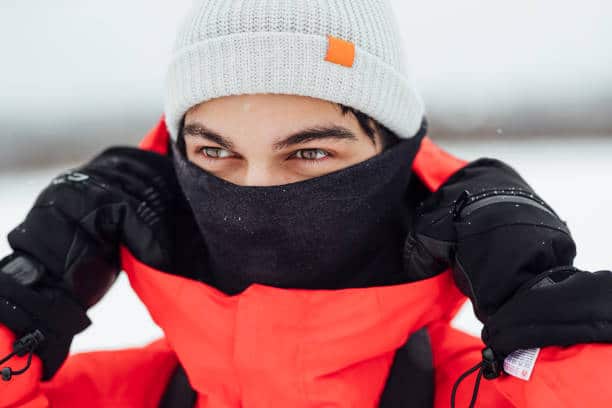 A caucasian man wearing warm winter clothing and accessories in a snowy, rural, outdoor setting.